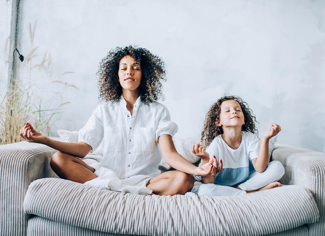 Wellness Benefit Plans - Mother and Daughter Meditating on the Coach in the Living Room